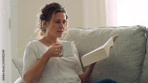 Woman reads book and sips from mug while reclining on couch with feet up photo
