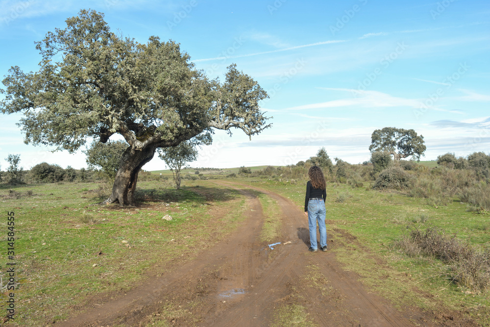 Woman walking on a dirt road in a landscape with vegetation and holm oaks