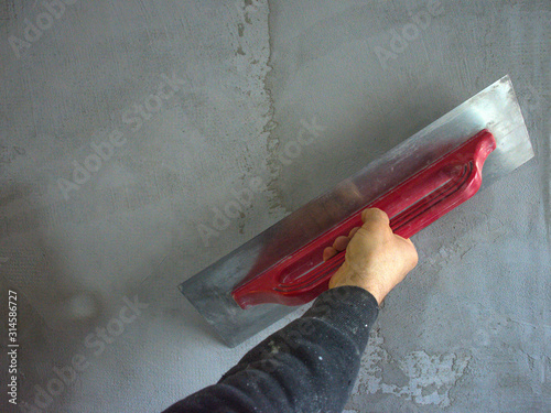 Worker hand plastering and smoothing concrete wall with cement and a steel trowel, on construction site photo