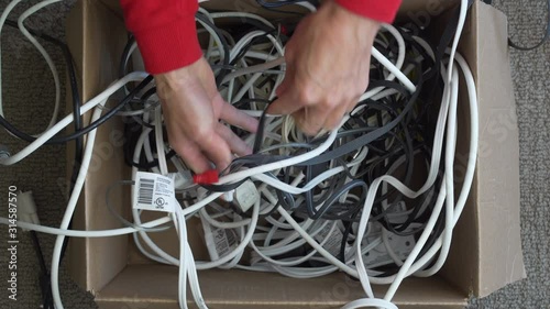 Top view of struggling hands attempting to untangle box of knotted cords photo