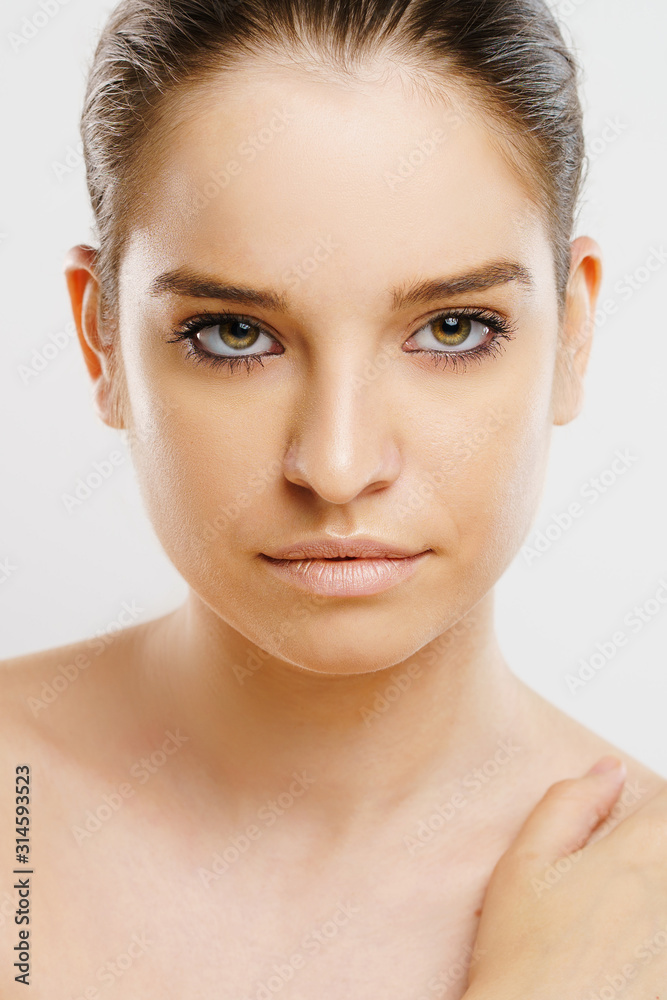 Beauty portrait of beautiful caucasian girl young brunette woman natural perfect skin and makeup holding hand on shoulder looking to the camera tied hair Beauty portrait of beautiful caucasian girl young brunette woman natural perfect skin and makeup holding hand on shoulder looking to the camera tied hair