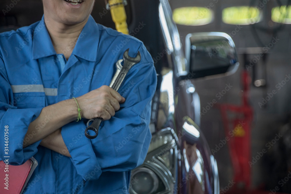 Mechanic in blue uniform hand with wrench at auto service garage . Auto mechanic in car repair