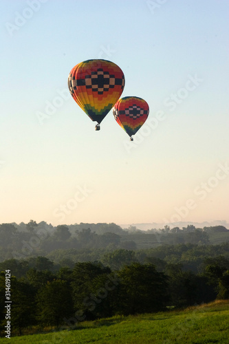 A pair of hot air balloons slide low over a wooded area during a flight in Iowa.