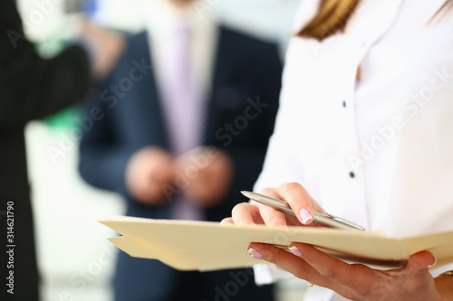 Focus on secretary with pretty manicure inspecting important business contract with concentration in modern office. Tender lady hands holding special pen. Company meeting concept. Blurred background