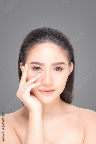 Beautiful Young Woman with clean fresh skin  Proposing a product. Gestures for advertisement on gray background.
