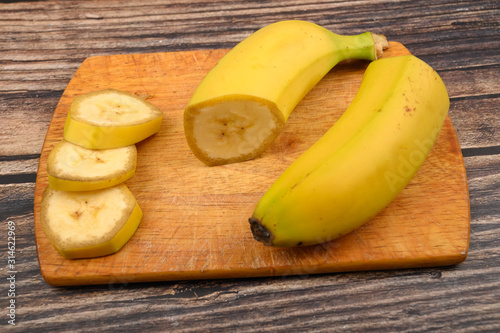 One ripe yellow banana cut into several pieces on a wooden Board on a wooden background. Close up.