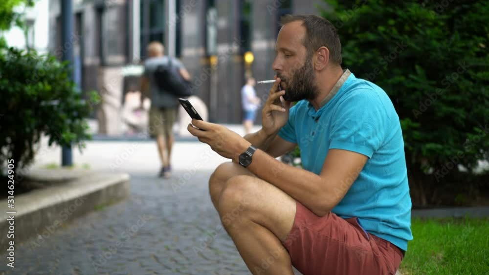 Young man with smartphone smoking cigarette in the city