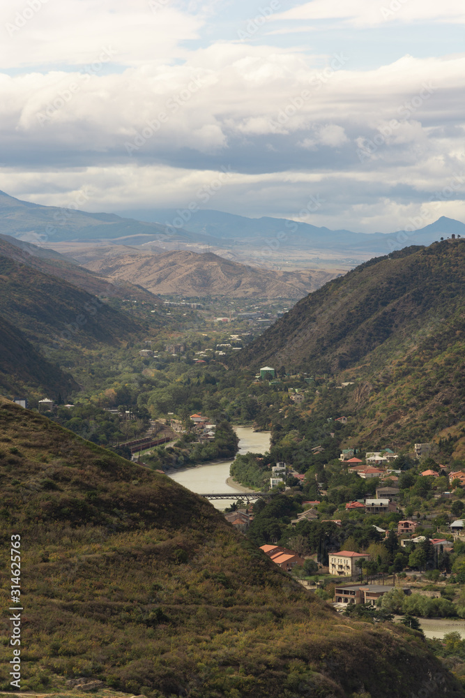 Fototapeta premium A magnificent view a valley surrounded by picturesque mountains, with numerous villages located along the river, over background of misty horizon and cloudy sky.