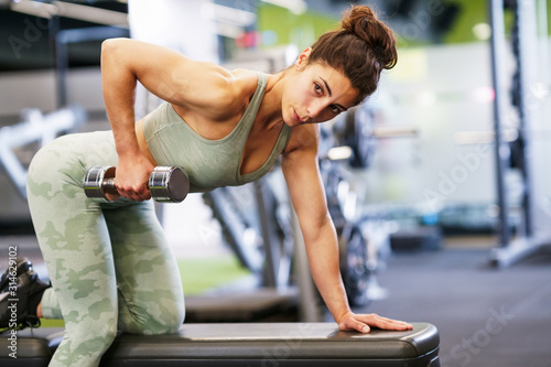 Woman working on her triceps and biceps in a gym with dumbbells