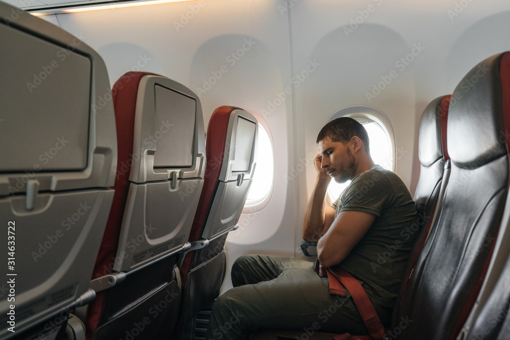 man sleeps in an airplane while sitting in a chair. Inconvenient and