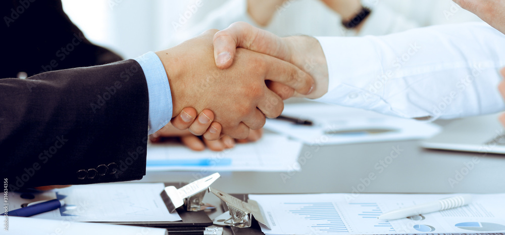 Business people shaking hands at meeting while theirs colleagues clapping and applauding. Group of unknown businessmen and women in modern white office. Success teamwork, partnership and handshake Business people shaking hands at meeting while theirs colleagues clapping and applauding. Group of unknown businessmen and women in modern white office. Success teamwork, partnership and handshake