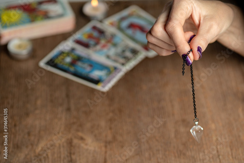 Arm of dowser with hand-held pendulum on the background of tarot cards. Selective focus. photo
