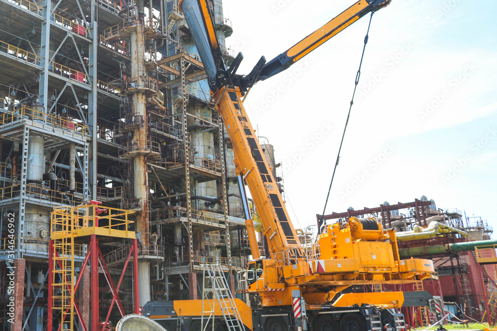 Construction and installation work with a powerful construction crane of a large new industrial oil refining petrochemical chemical plant with pipes, columns, railings, stairs and equipment Construction and installation work with a powerful construction crane of a large new industrial oil refining petrochemical chemical plant with pipes, columns, railings, stairs and equipment