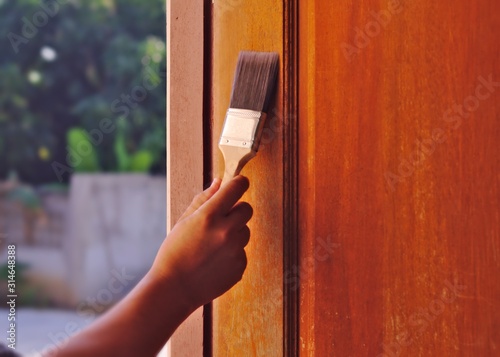 Hand painted brush painter brown wooden door Bright sunlight tree exterior background Work day House construction Workers Painters Painting surface coating Front door