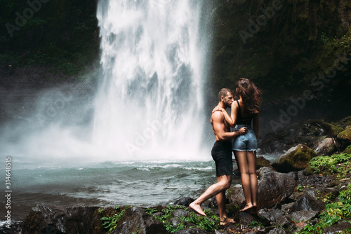 A man of athletic build kisses a beautiful girl at the waterfall. Honeymoon trip. Declaration of love. A couple in love on a waterfall. Happy couple in Bali. Beautiful couple travels the world