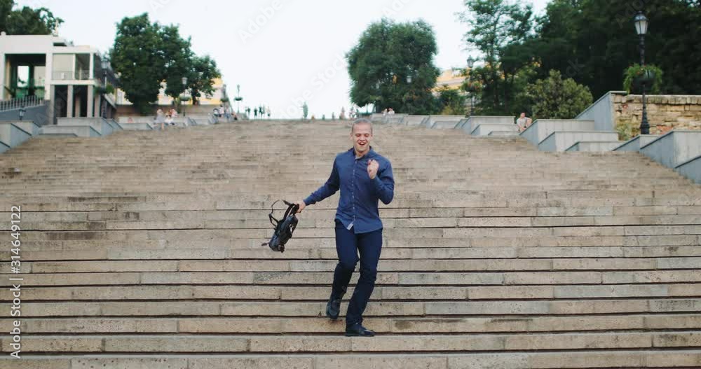 Handsome guy with phone dances on stone stairs receiving good business news at sunset light in summer city Handsome guy with phone dances on stone stairs receiving good business news at sunset light in summer city