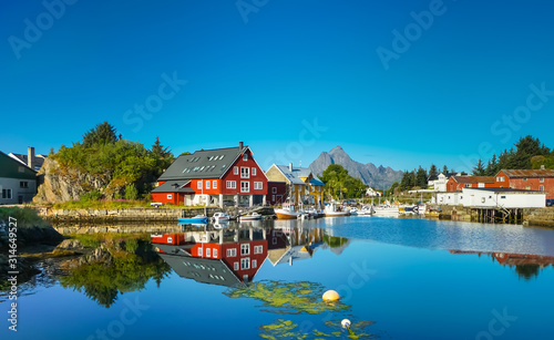 Village on the shore of the fjord, Lofoten Islands, Norway. Sunny day, clear blue sky, colorful house, reflection in the water, forest and mountains in the background. photo