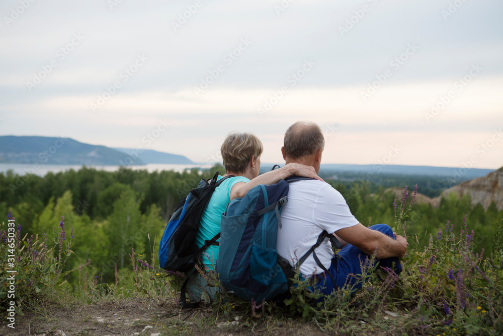 Quality Time. elderly couple with backpacks sits on the mountain. Senior couple walking in nature. Outdoor activities on weekends. St. Valentine's Day Quality Time. elderly couple with backpacks sits on the mountain. Senior couple walking in nature. Outdoor activities on weekends. St. Valentine's Day