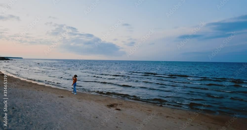 A lonely girl walks on the beach by the North sea. Gloomy sky and cold blue atmosphere. Misty Lake in vintage Scandinavian style. Ladoga in Leningrad Oblast, Russia. Aerial view of seascape. 4K flying A lonely girl walks on the beach by the North sea. Gloomy sky and cold blue atmosphere. Misty Lake in vintage Scandinavian style. Ladoga in Leningrad Oblast, Russia. Aerial view of seascape. 4K flying