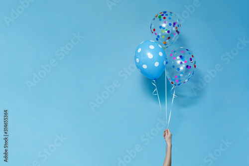 stylish birthday party or holidays with balloons close up. blue  balloons isolated  on the blue background with copy space for text. Hand  holding three bright colorful balloons indoor.