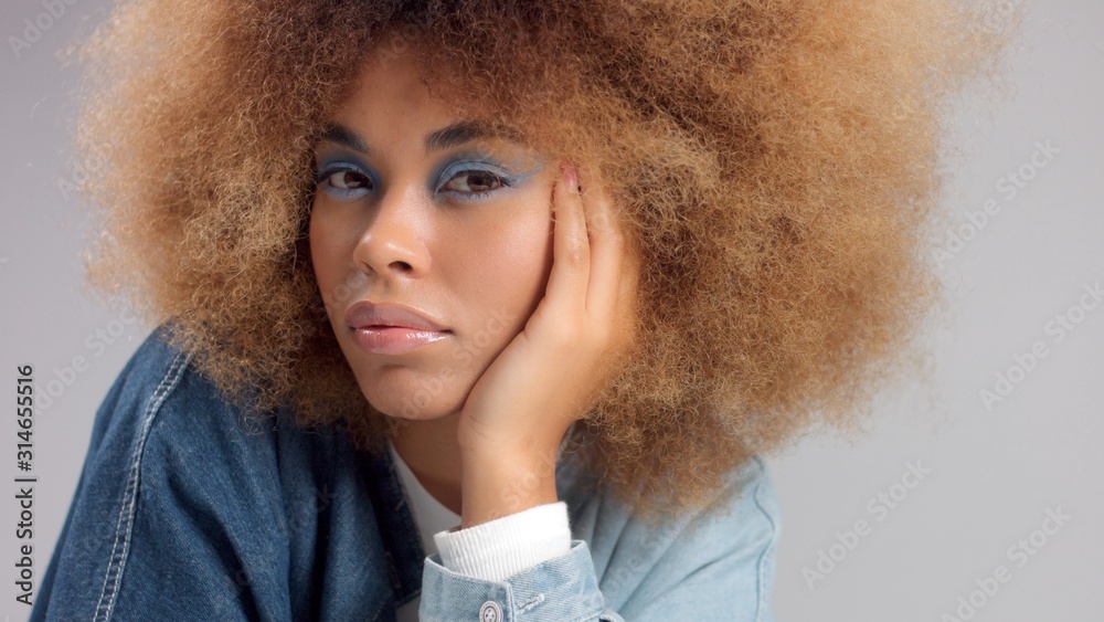 closeup of mixed race black woman in denim oversized shirt and huge afro hair watching to the camera with light blue eye makeup. Z generation - obrazy, fototapety, plakaty 