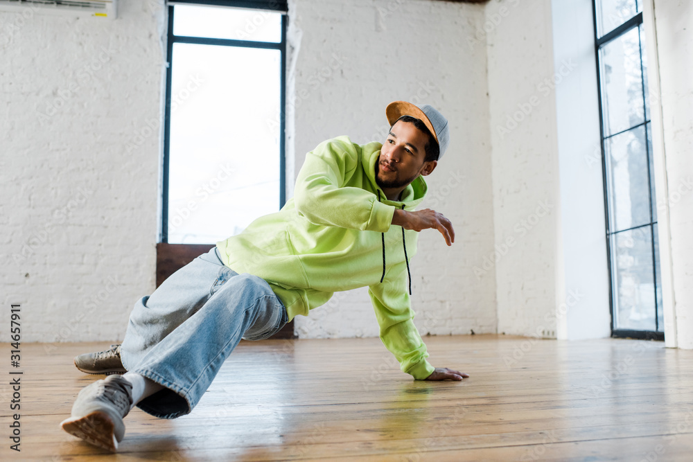 stylish african american man in cap breakdancing in dance studio