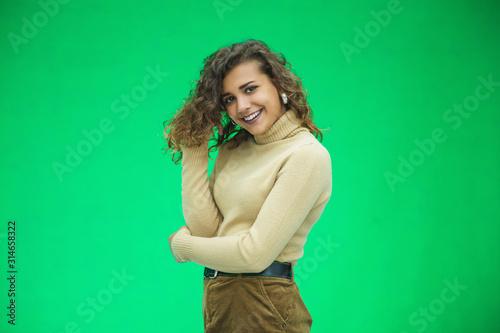 Beautiful woman with kinky hair in beige clothes, isolated on green, looking pleased. © Andrii