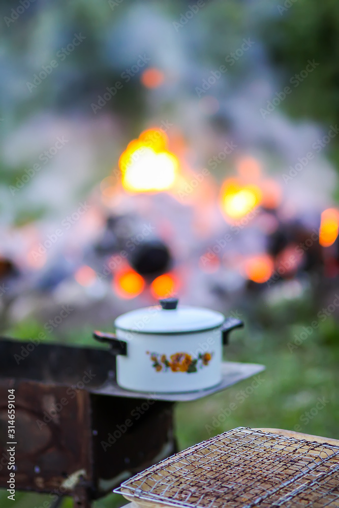 Meat on the grill and white pan on the brazier on bonfire background Meat on the grill and white pan on the brazier on bonfire background