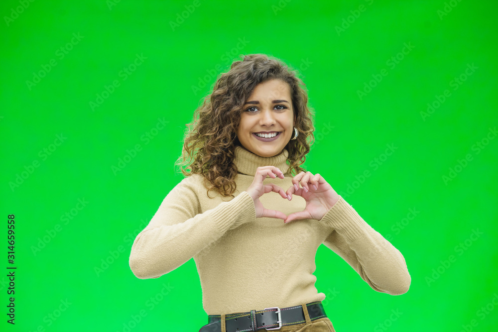Gorgeous young woman over a green background doing a heart shape with her hands. Gorgeous young woman over a green background doing a heart shape with her hands.