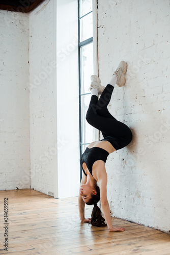 young woman doing handstand near brick wall in dance studio