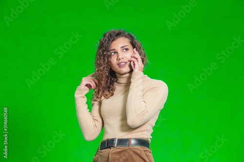 Friendly female talking on her cell phone, standing against green background. © Andrii
