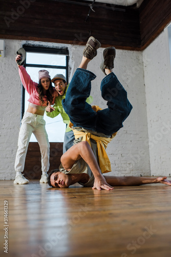 selective focus of handsome man breakdancing near excited multicultural dancers
