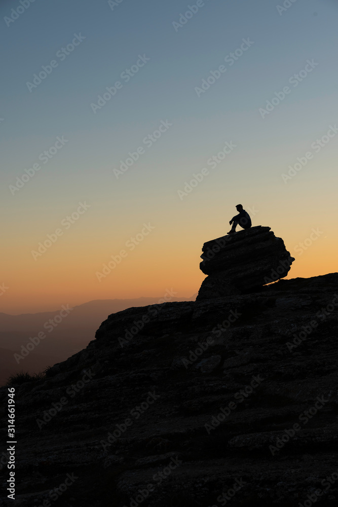 silhouette of man on stones looking down while it is getting dark