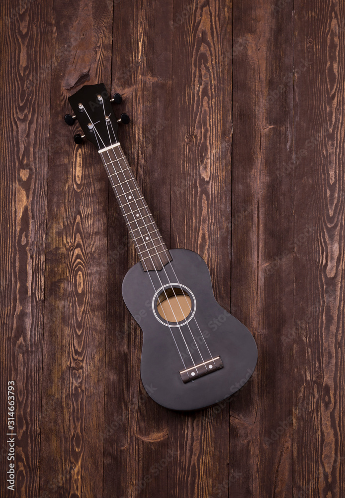 Naklejka premium Ukulele black top view on a wooden background. Classic ukuleles, great design for any purpose.