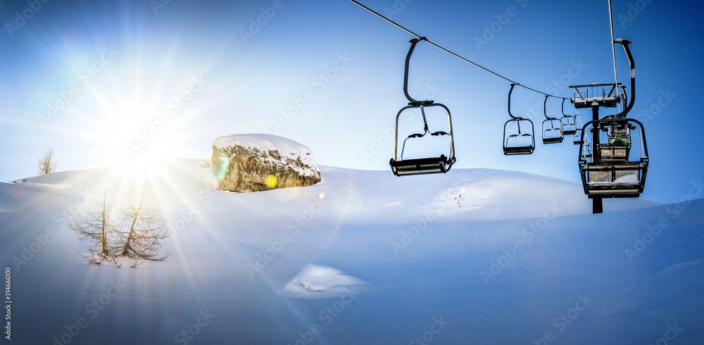 Ski lift seats high in the mountains. Winter elevator mountains panorama with sun and blue sky in background.