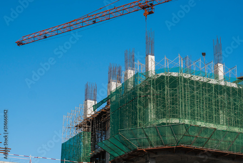 Crane and building construction site against blue sky. Metal construction of unfinished building on construction. Tower Crane use for building of multi storage building. photo