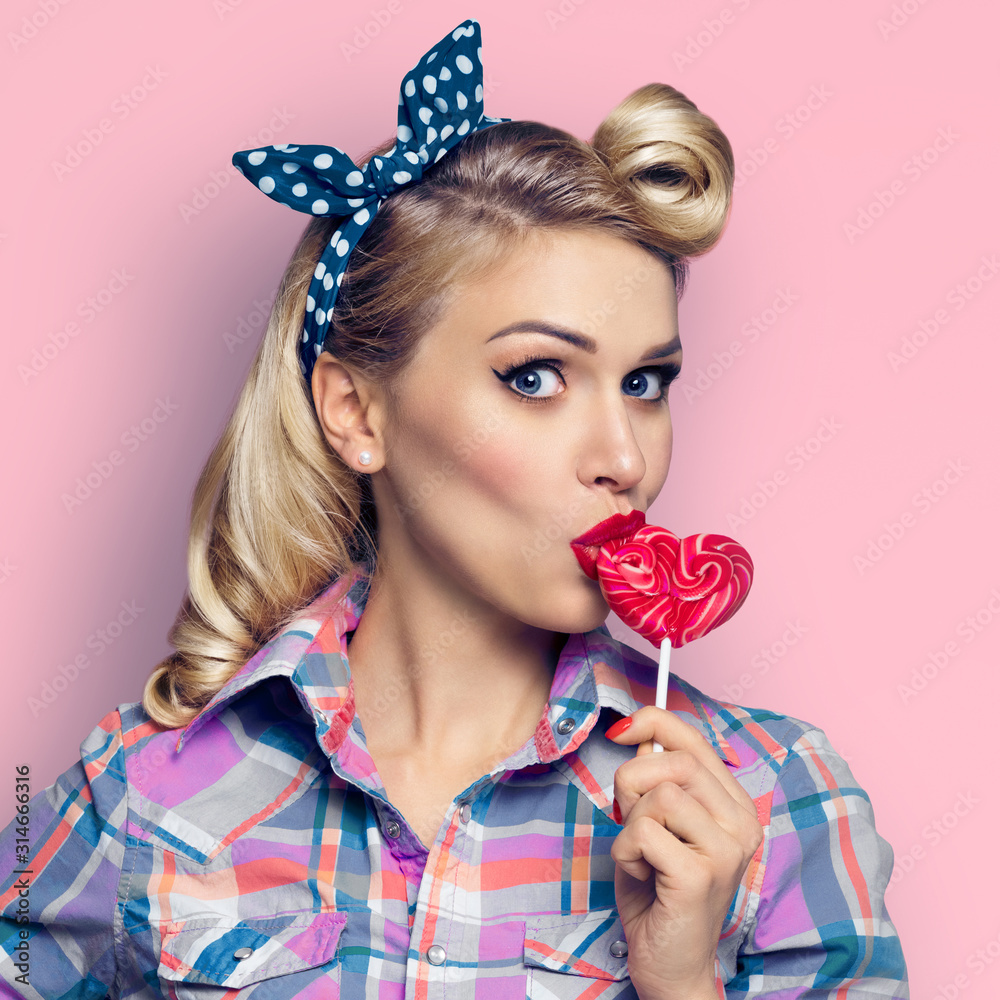 Surprised woman eating heart shape candy lollipop. Girl in pin up ...