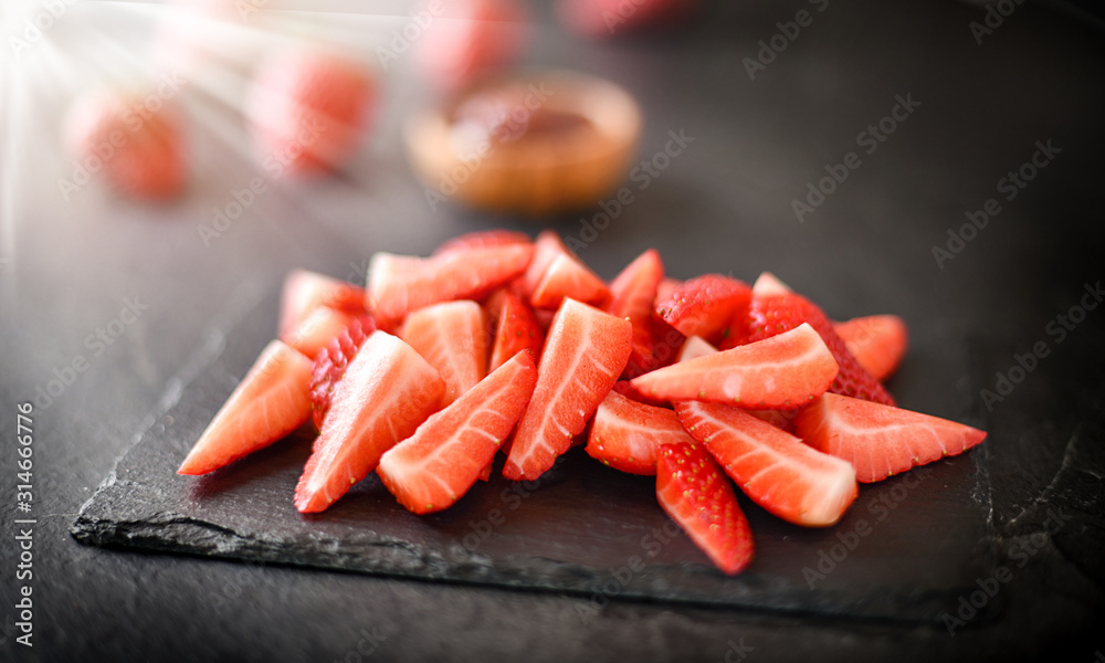 Finest fresh cut pieces of strawberries on dark stone slate. Juicy strawberry red fruits top view at black background. Finest fresh cut pieces of strawberries on dark stone slate. Juicy strawberry red fruits top view at black background.