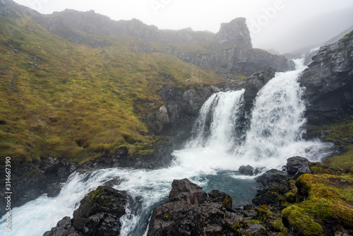 Klifbrekkufossar waterfall in the eastern part of Iceland during rainy and foggy weather. Moss covered landscape and basalt rocks. Icelandic and weather concept.