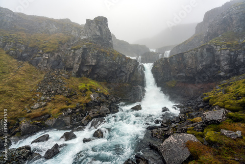 Klifbrekkufossar waterfall in the eastern part of Iceland during rainy and foggy weather. Moss covered landscape and basalt rocks. Icelandic and weather concept.