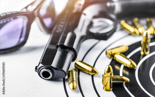 Hand gun detail with ammunition on paper target. 9 mm pistol gun weapon and bullets at dark background.