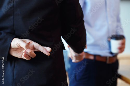 Business partners shaking hand making a deal but Business man holding crossed fingers behind back, Betray concept.