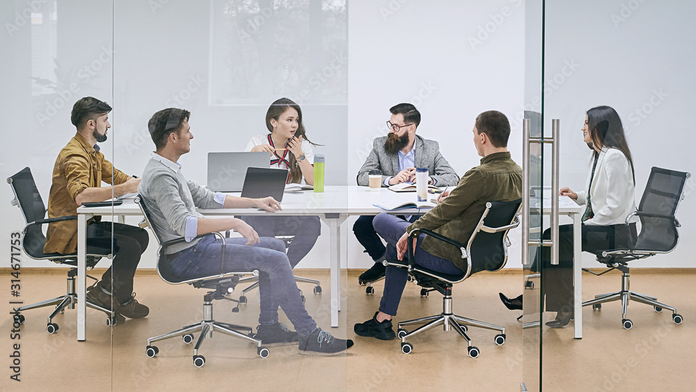 Corporate business team and manager in a meeting at IT company office conference room. View through glass wall.