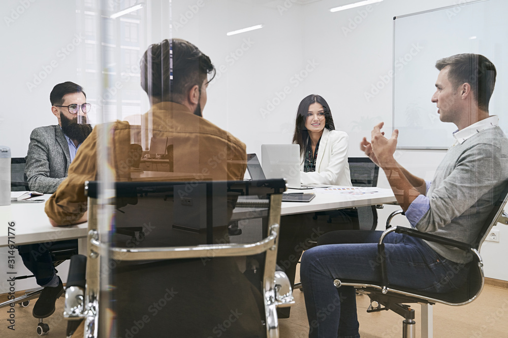 Corporate business team and manager in a meeting at IT company office conference room. View through glass wall.