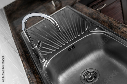 Close up on modern kitchen metal faucet and metal kitchen sink.