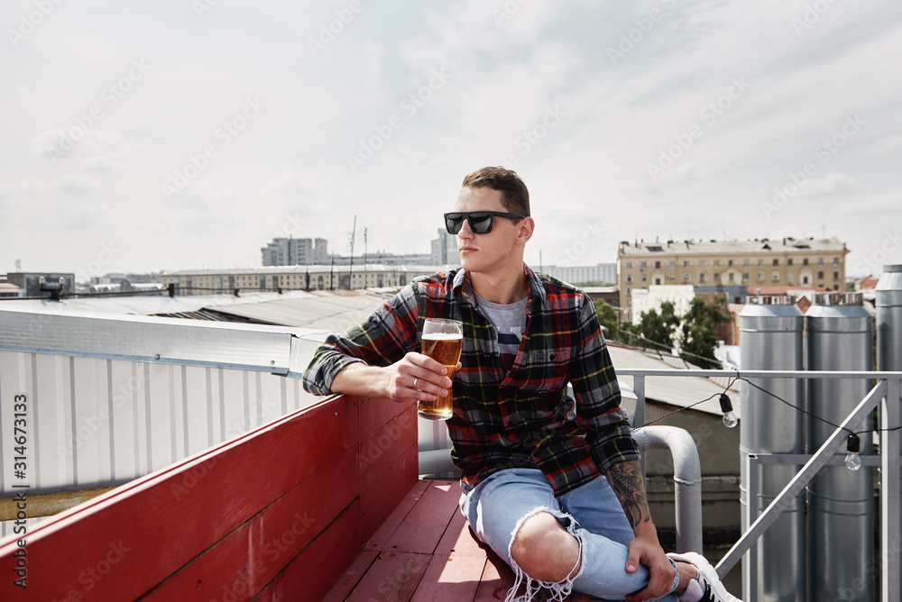 Happy man in eyewear drinking beer at bar or pub on roof, copy space