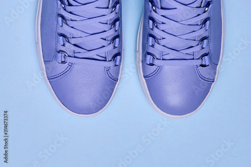 Stylish violet female shoes on blue pastel background, copy space. New sneakers. Beauty and fashion concept. Flat lay, top view. Overhead shot
