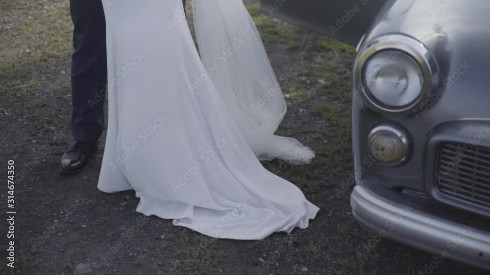 Legs of groom and bride in wedding dress next to oldtimer car, medium shot