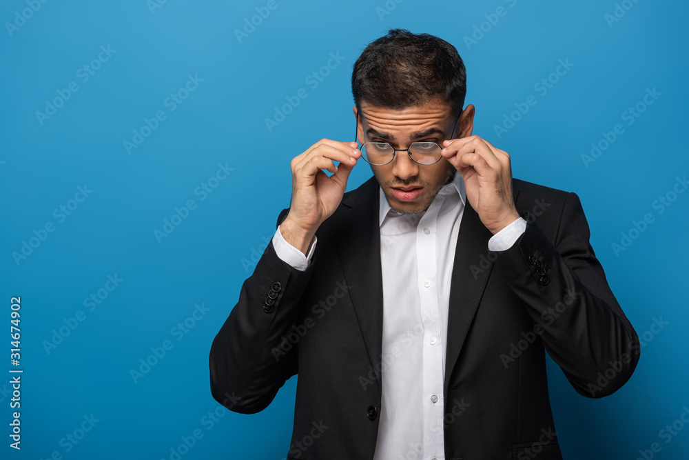 Handsome businessman adjusting eyeglasses on blue background Handsome businessman adjusting eyeglasses on blue background