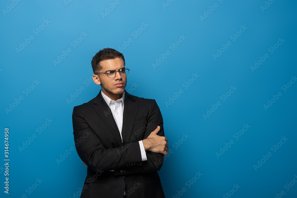 Sceptical businessman with crossed arms looking away on blue background Sceptical businessman with crossed arms looking away on blue background